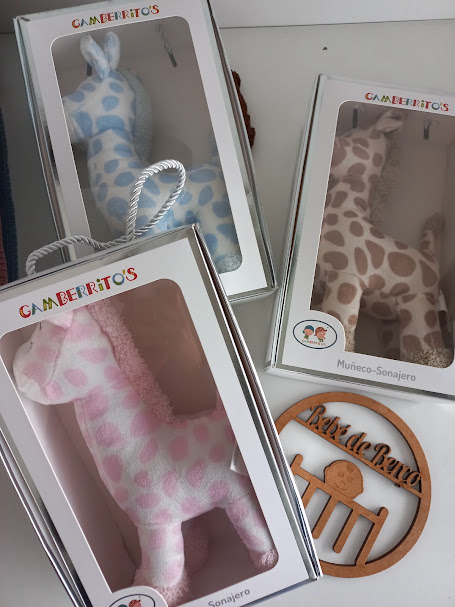 Brinquedos sonâjeros em embalagem branca e um ornamento de madeira sobre mesa branca.