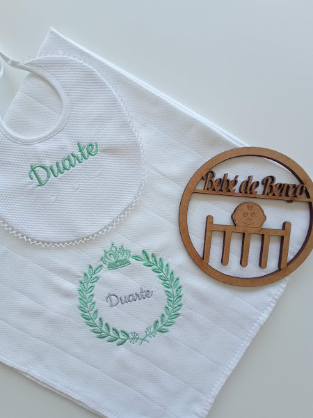 Babete e toalha brancos bordados com o nome Duarte e placa de madeira 'Bebé de Berço'.