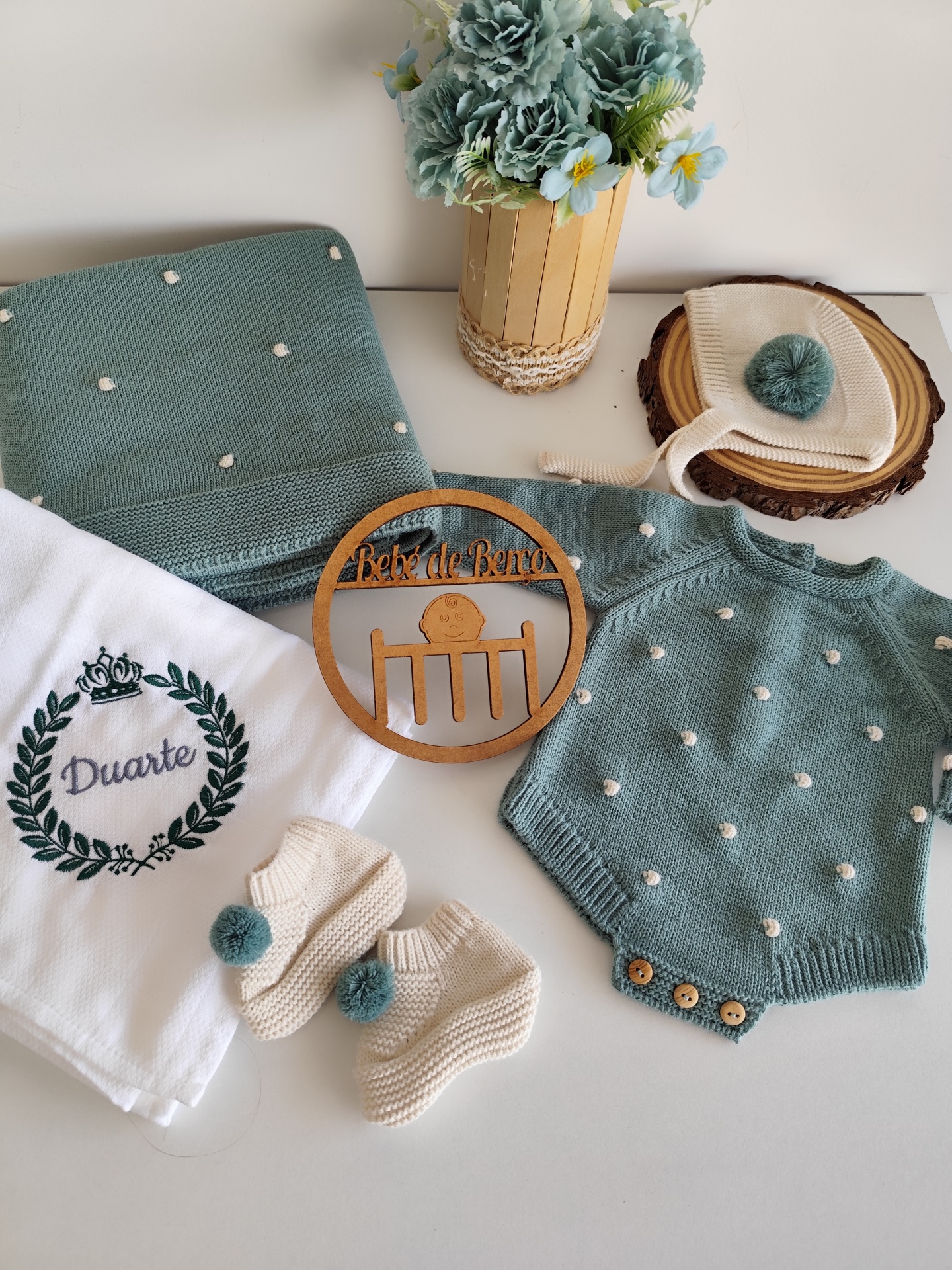 Conjunto de roupa de bebé verde e creme com toalha branca bordada e flor num vaso