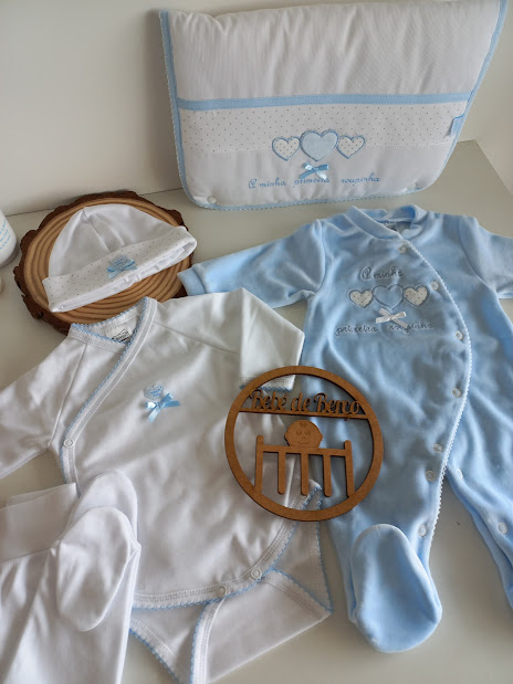 Roupa de bebé azul e branca com bordados e placa de madeira com texto