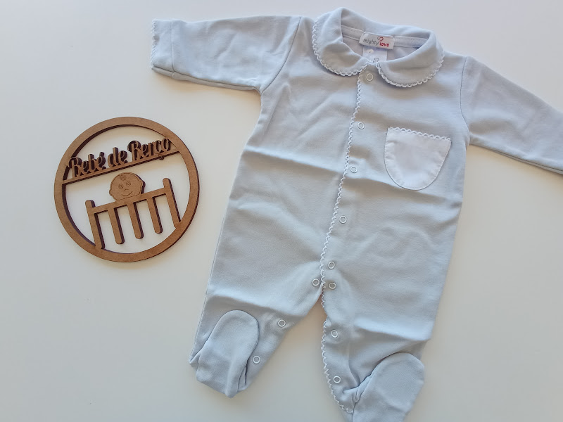 Macacão branco para bebé com gola bordada e bolsinho, em superfície branca ao lado de ornamento de madeira