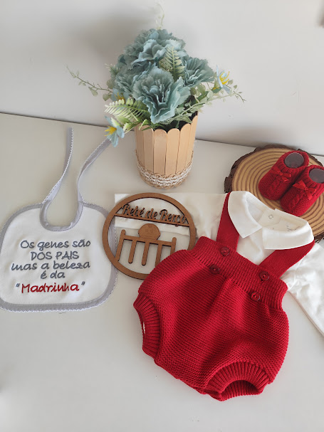 Conjunto de roupa de bebé com babete, jardineira vermelha, body branco, sapatinhos vermelhos e vaso com flores azuis