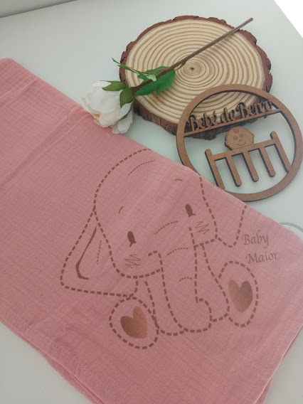Toalha rosa para bebé com padrão de elefante e objeto decorativo de madeira.