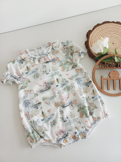 Conjunto de bebé branco com padrão de animais e bicicletas, gola com folho e botões na zona da fralda.
