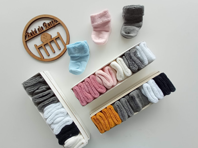 Caixas abertas com meias de bebé coloridas e uma placa de madeira redonda com texto