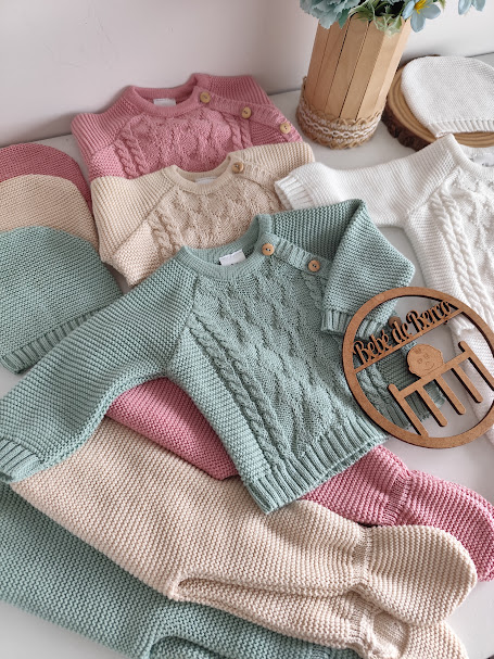 Conjunto de roupa de bebé em malha tricotada com blusas e calças em tons pastel dispostas sobre mesa branca