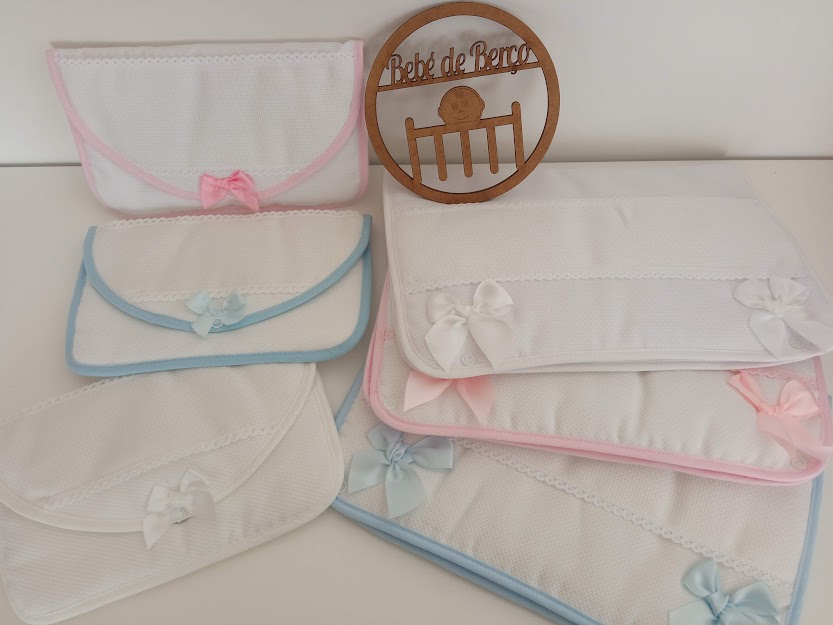 Fraldas brancas com bordas coloridas e laços, placa de madeira com texto