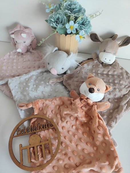 Quatro paninhos de pelúcia com cabeça de animal e textura de bolinhas junto a vaso com flores azuis