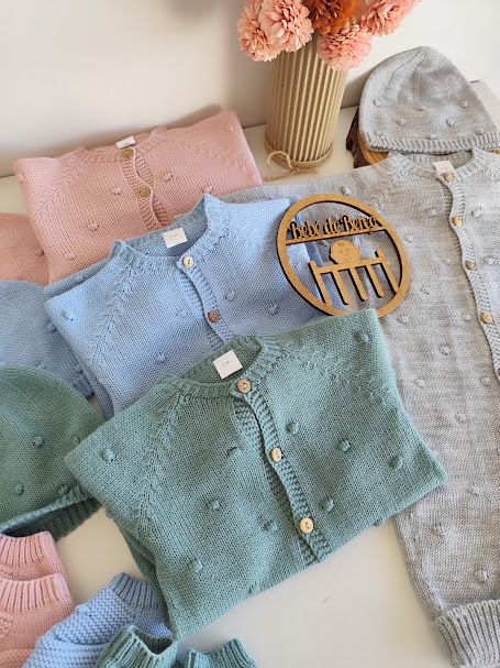 Conjunto de roupa de bebé em malha em várias cores com botões, toucas e um vaso de flores cor de rosa