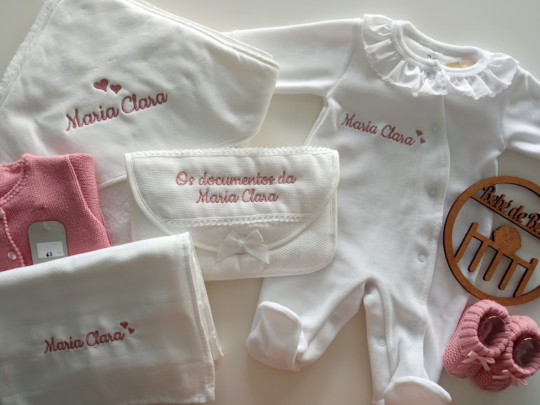 Conjunto de roupa e acessórios para bebé em branco e rosa com nomes bordados e porta-documentos com laço.