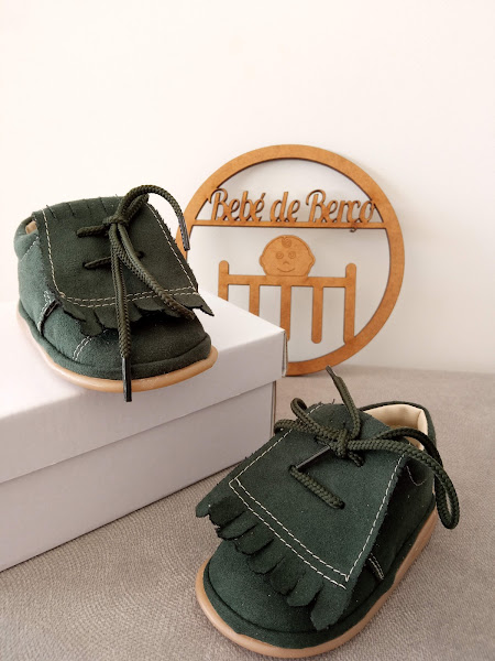 Sapatos de bebé em camurça verde escura com franjas e atacadores sobre caixa branca