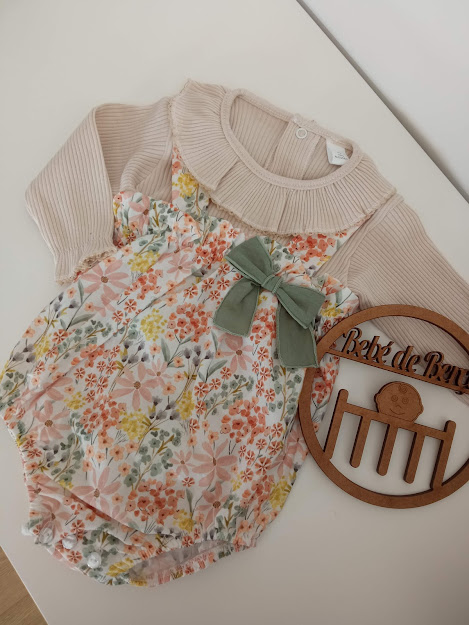 Body de bebé floral com mangas longas bege e laço verde ao lado de moldura de madeira