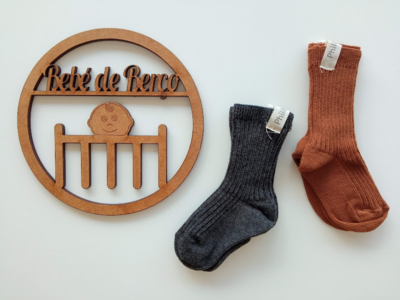 Dois pares de meias infantis com etiqueta PHIL, ao lado de placa decorativa Bebé de Berço de madeira