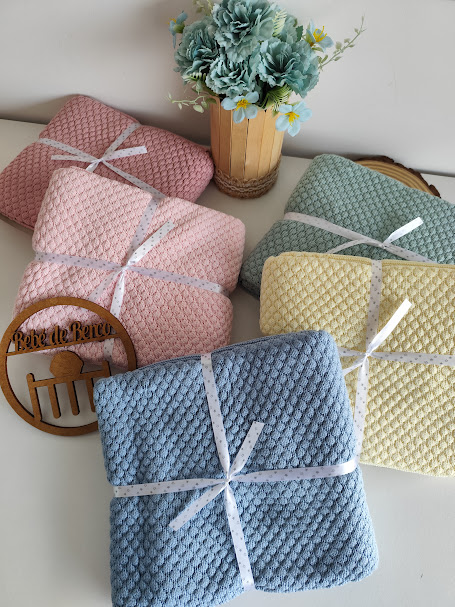 Mantinhas de bebê texturizadas em várias cores com fita branca, vaso de flores e placa de madeira