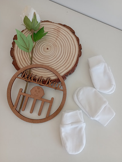 Luvas brancas para bebé e decoração de madeira com frase 'Bela de Berço' sobre disco de madeira