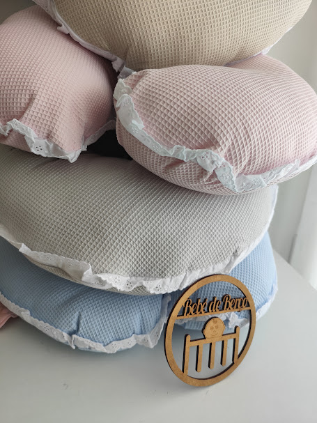 Almofadas redondas coloridas com textura e bordas de renda, sobre uma superfície branca, com placa de madeira com inscrição