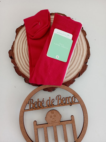 Meias vermelhas com etiqueta verde em disco de madeira e ornamento de bebé de berço