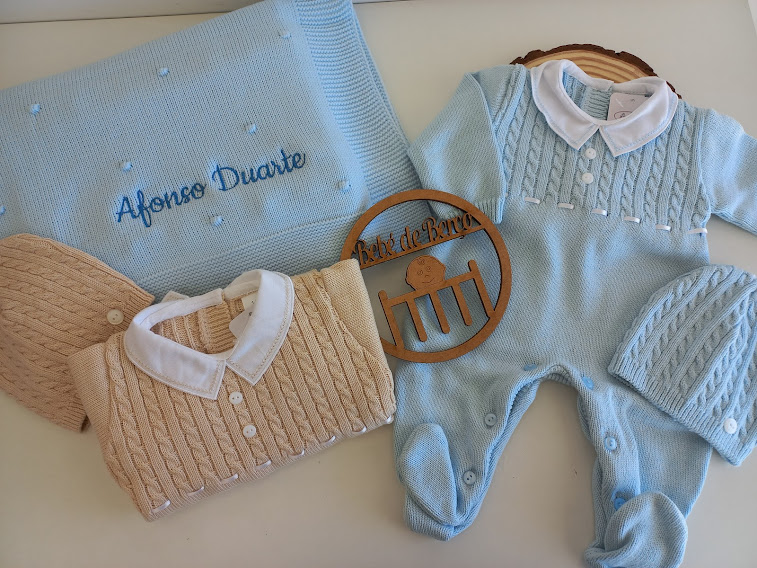 Conjunto de roupa e acessórios de bebé em malha azul e bege com manta bordada e decoração de madeira