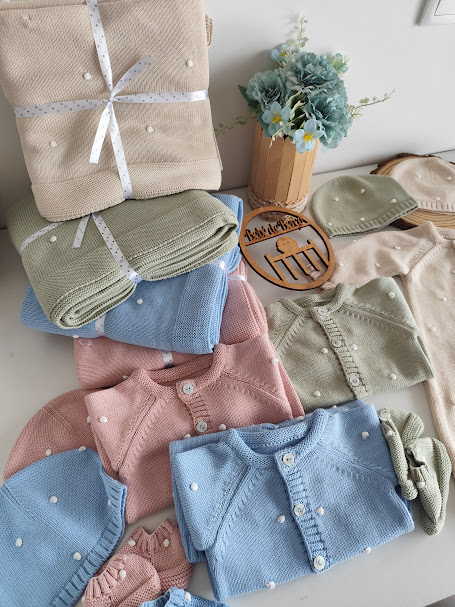 Conjunto de roupa de bebê colorida em malha com textura de pontos em relevo e acessórios sobre uma superfície branca