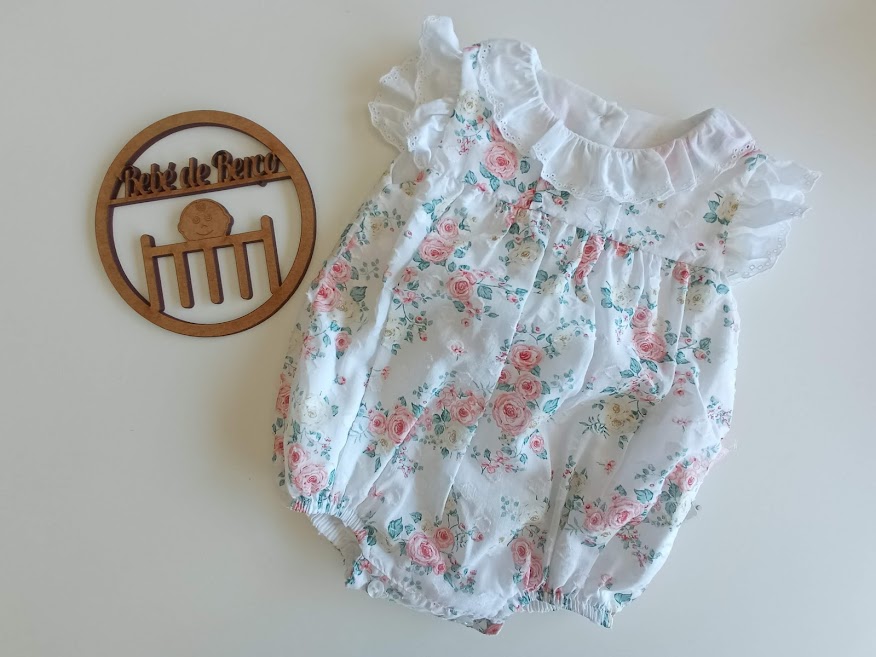 Body de bebé branco com padrão floral e folhos ao lado de placa decorativa de madeira