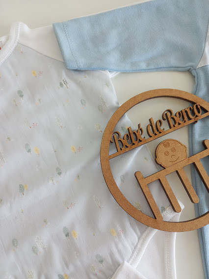 Roupa de bebé com mangas azul claro e branca com padrão, e objeto decorativo de madeira