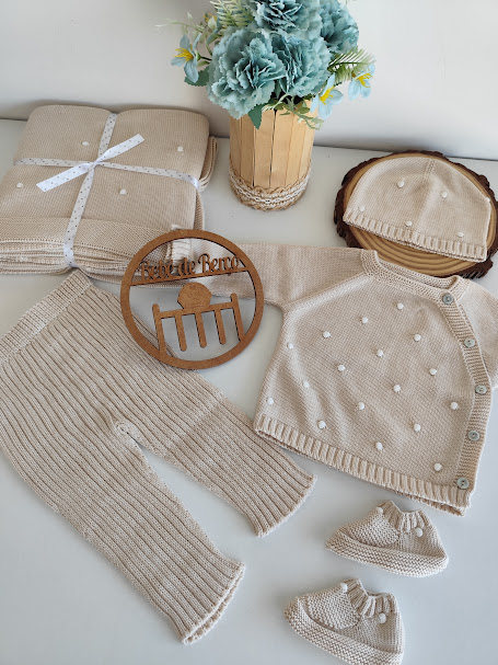 Conjunto de roupa de bebé em tricô bege com pérolas e acessórios sobre superfície branca