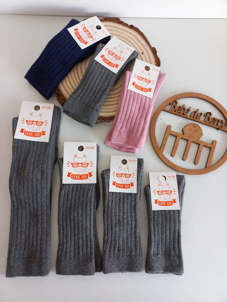 Sete pares de meias caneladas com etiquetas com desenho de gato e texto COOL KID sobre superfície branca e objeto de madeira