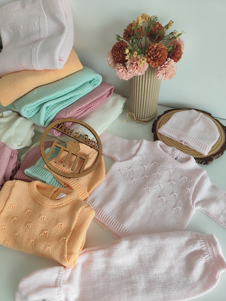 Roupas de bebé em malha coloridas pastéis com padrões delicados e vaso com flores secas