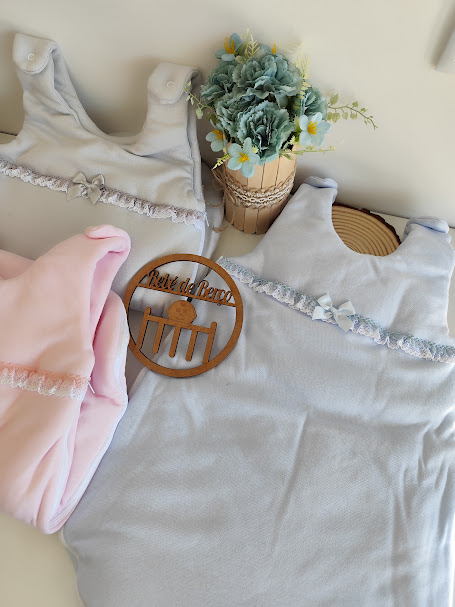 Sacos de dormir de bebé em cinza e rosa com rendas, flores artificiais e enfeite de madeira com texto Ateliê da Pinto