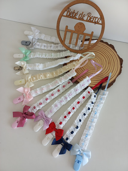 10 prendemamas rendados com laços coloridos e presilhas, sobre superfície branca e base de madeira redonda com texto em madeira.