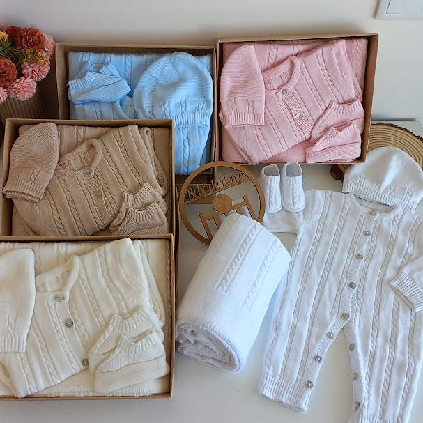 Conjunto de roupa de bebé tricotada em tons pastel com cardigans e macacão branco com capuz.
