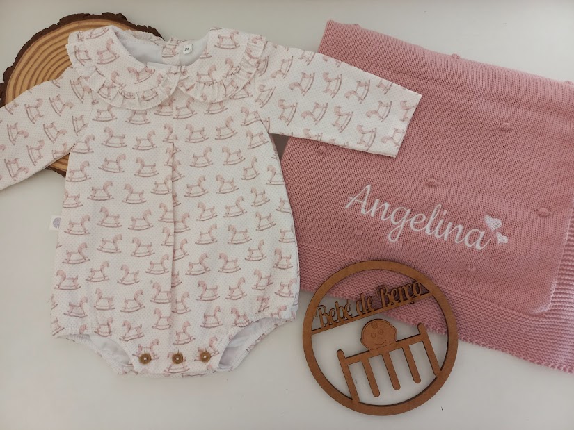 Body de bebé branco e rosa com padrão de cavalinho de pau, manta rosa com nome 'Angelina' bordado e círculo de madeira gravada