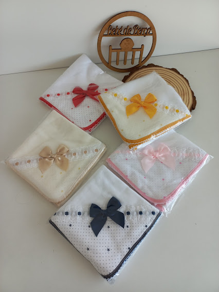 Cinco toalhas brancas com laços coloridos e bordas decorativas, com uma placa de madeira com texto ao fundo.