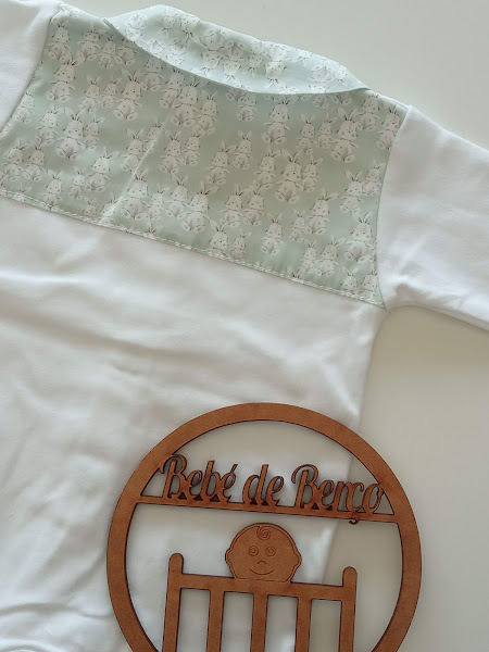 Babygrow branco com parte superior verde com padrão de coelhos e placa de madeira com texto Bebé de Berço