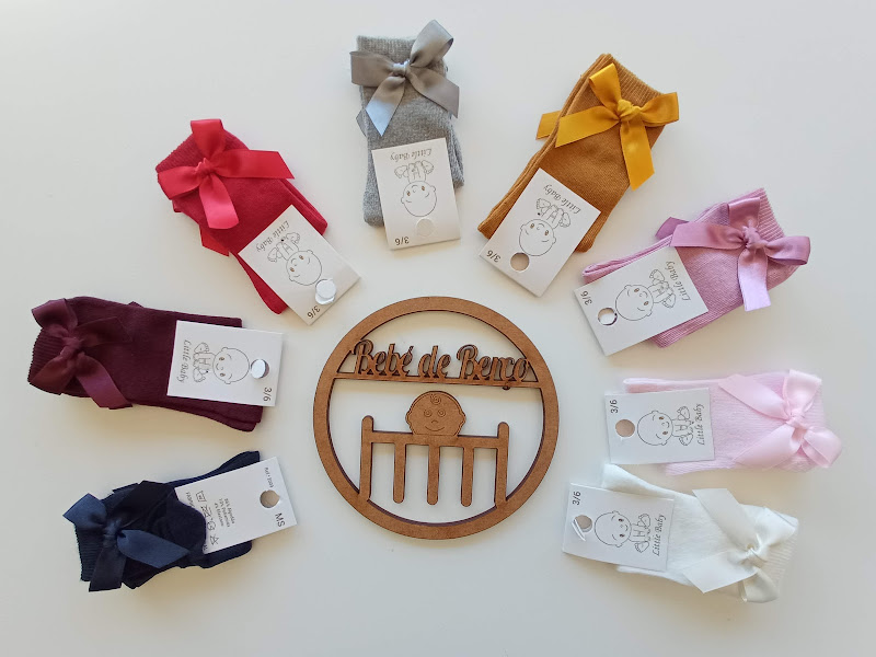 Collants para bebé coloridos com laços e etiquetas dispostos em círculo com um emblema de madeira ao centro