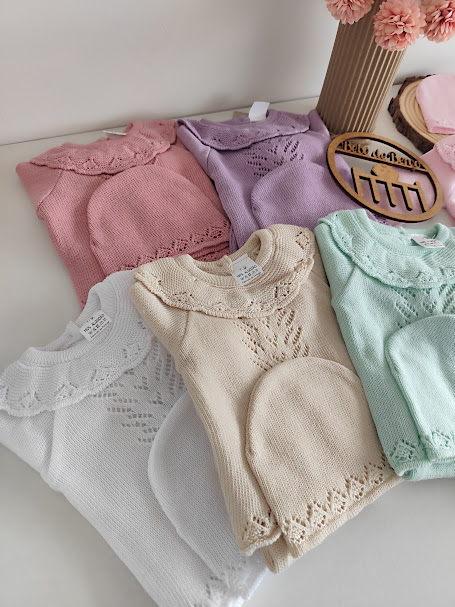 Conjuntos de roupa de bebê em malha com colarinhos rendados em várias cores sobre superfície branca.