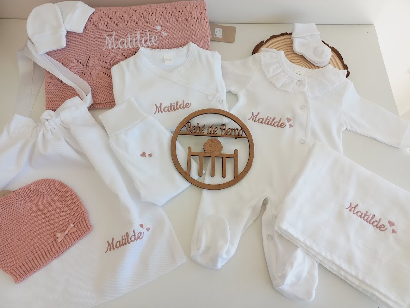 Conjunto de roupa de bebé com nome Matilde bordado, em branco e rosa, com várias peças e manta.