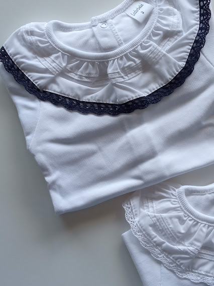 Macacões brancos de bebé com gola frisada e renda preta ou branca.