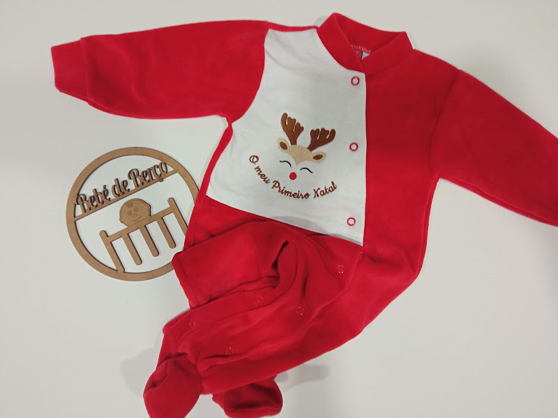 Macacão de bebé vermelho e branco com estampa de rena e texto O meu Primeiro Natal, sobre superfície branca com decoração de madeira Petit de Pierre