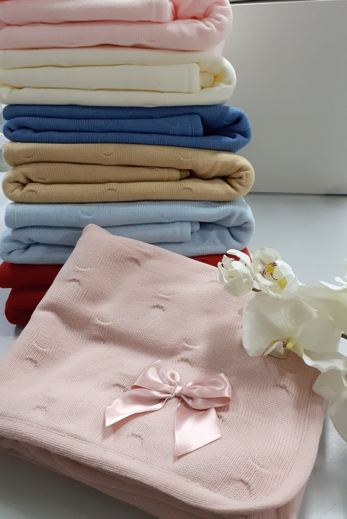 Cobertores de malha empilhados com laço rosa e flor branca ao lado