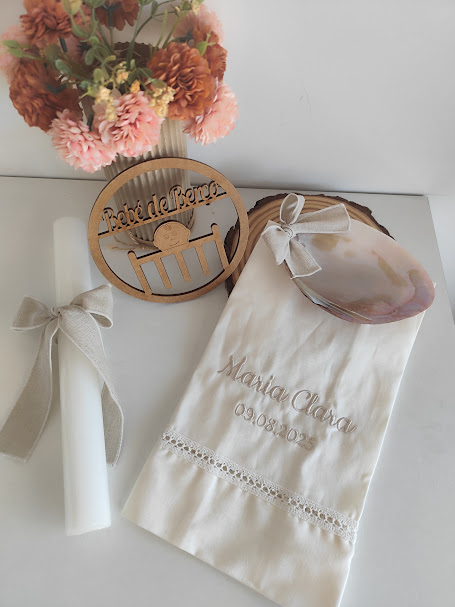 Flores, castiçal de madeira, vela, concha e toalha bordada em superfície branca