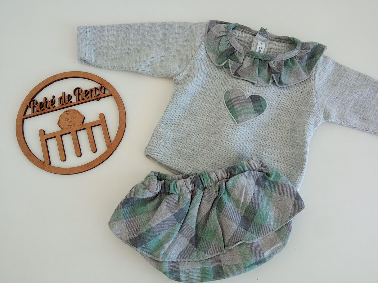 Conjunto de roupa de bebé com camisola cinzenta e saia xadrez em tons verde e cinza sobre fundo branco.
