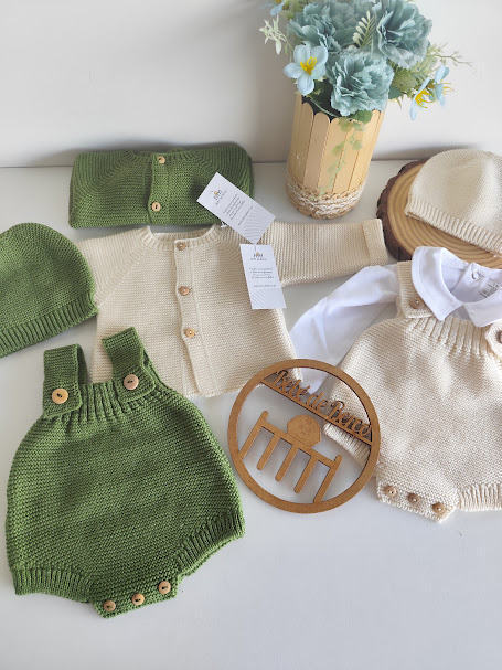 Conjunto de roupa de bebé em malha verde e creme com acessórios, junto a vaso com flores