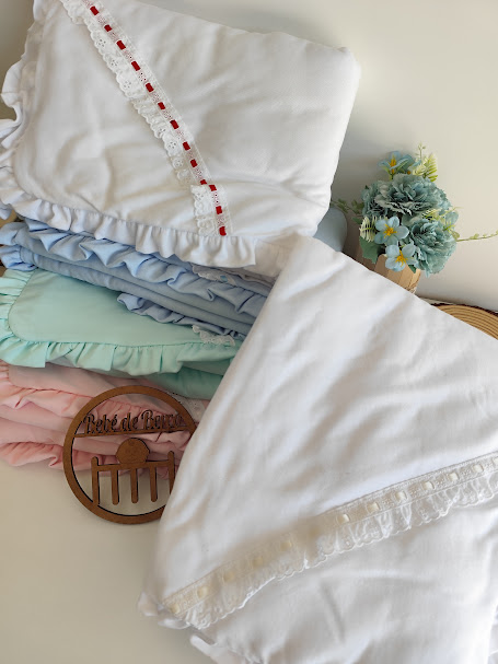 Mantas para bebé em várias cores com folhos e renda, peça de madeira gravada e vaso com flores artificiais.