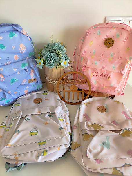 Quatro mochilas infantis coloridas com padrões e nome CLARA, vaso com flores e ornamento de madeira