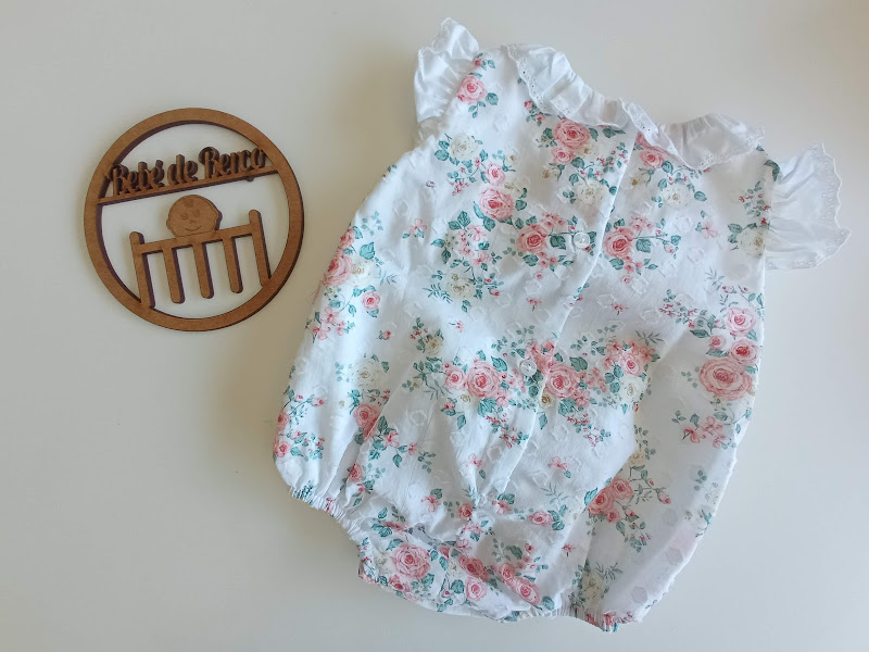 Body de bebé floral branco com gola e mangas curtas ao lado de placa de madeira 'A Vida de Franco'