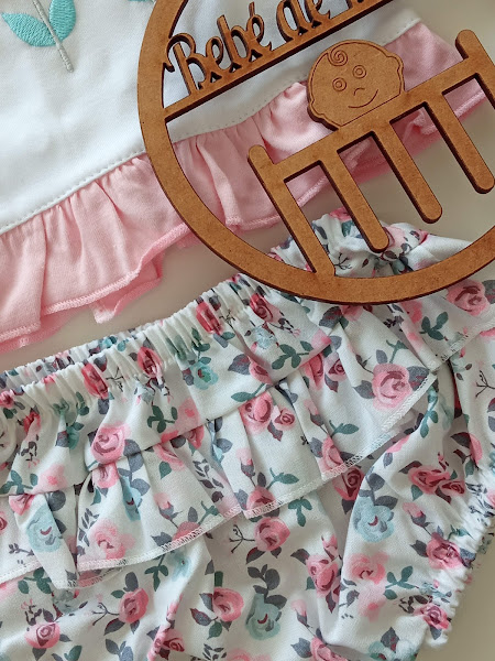 Roupas de bebé com padrão floral e objeto de madeira com texto recortado