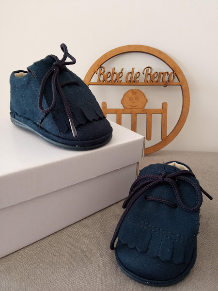 Sapatos de bebé azuis escuros em camurça com atacadores pretos e franjas, com caixa branca e placa de madeira 