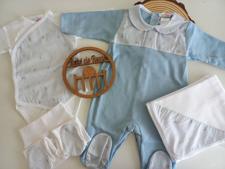 Conjunto de roupa de bebé branco e azul claro com sapatinhos e cobertor em fundo claro