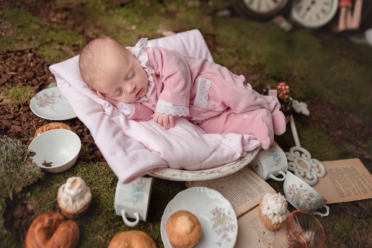 Bebé vestido de rosa dorme numa almofada rodeado por pratos e pães em ambiente natural